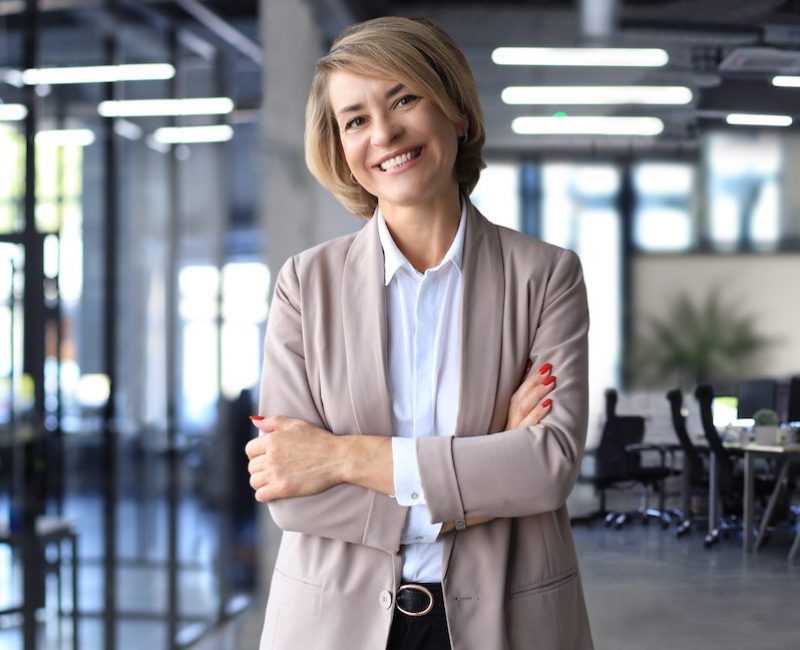 Confident stylish european middle aged woman standing at workplace, executive leader manager looking at camera